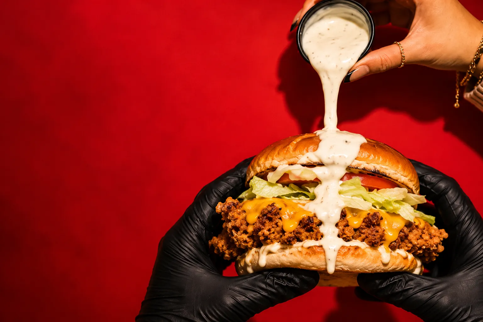 Salsa cayendo sobre una burger de pollo crujiente con cheddar, lechuga y tomate